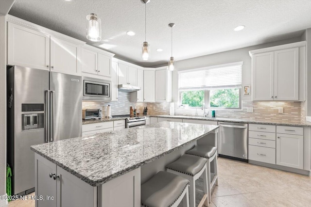 kitchen with a center island, recessed lighting, a textured ceiling, appliances with stainless steel finishes, and backsplash