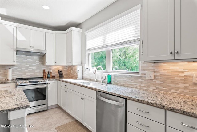 kitchen featuring under cabinet range hood, white cabinets, tasteful backsplash, light tile patterned floors, and stainless steel appliances
