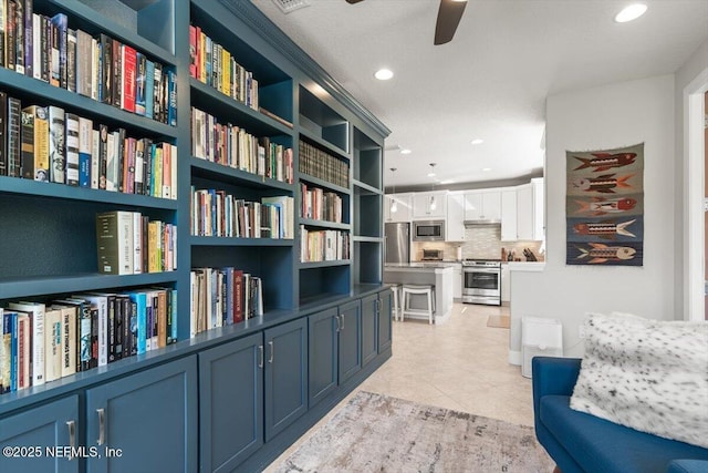 sitting room with recessed lighting, ceiling fan, light tile patterned floors, and wall of books