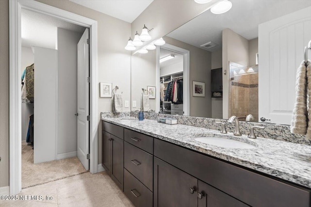 bathroom with a tile shower, a sink, double vanity, a spacious closet, and visible vents