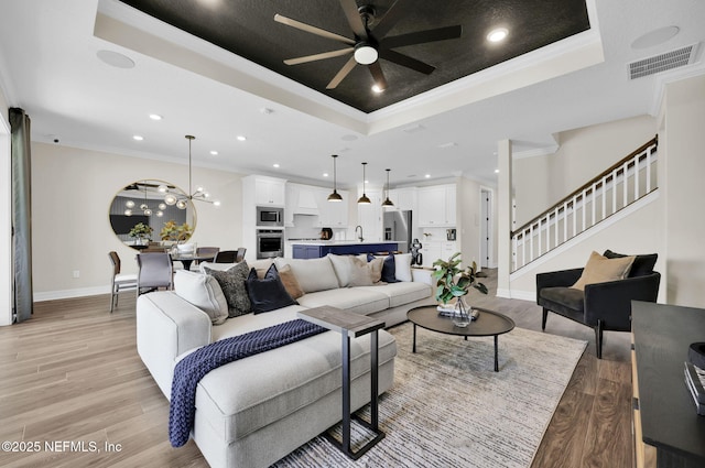 living room with ornamental molding, a tray ceiling, light wood finished floors, and visible vents