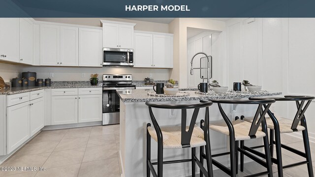 419 Seaport Breeze Rd, Saint Augustine, FL 32095 - kitchen with light stone countertops, a kitchen breakfast bar, stainless steel appliances, white cabinetry, and a center island with sink