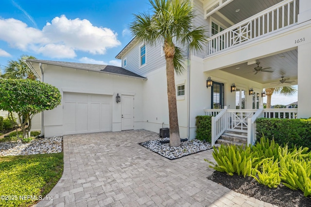 exterior space featuring a garage, ceiling fan, a balcony, decorative driveway, and stucco siding