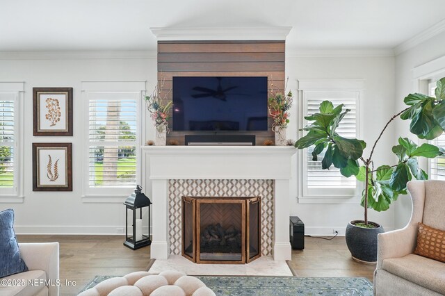 living area featuring a healthy amount of sunlight, crown molding, a tile fireplace, and wood finished floors