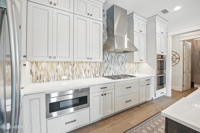 kitchen featuring wall chimney range hood, visible vents, white cabinets, light wood finished floors, and stainless steel appliances