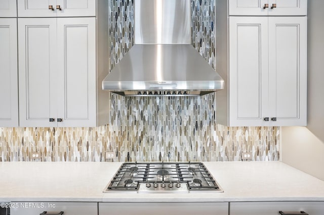 interior details with stainless steel gas cooktop, white cabinetry, wall chimney exhaust hood, and light countertops