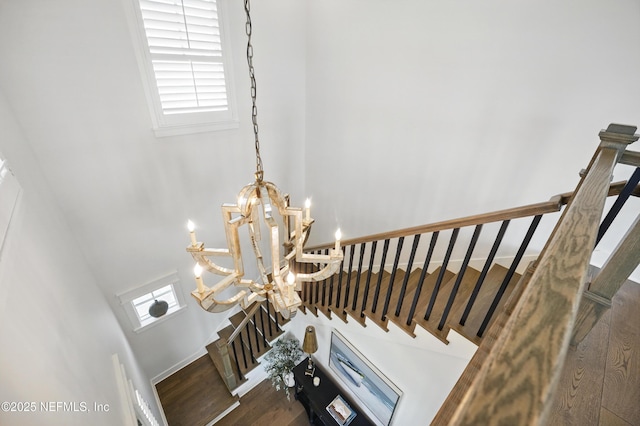 stairway featuring an inviting chandelier, plenty of natural light, wood finished floors, and a towering ceiling