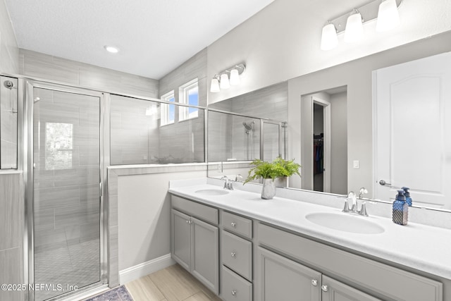 bathroom featuring double vanity, a sink, a stall shower, and a spacious closet