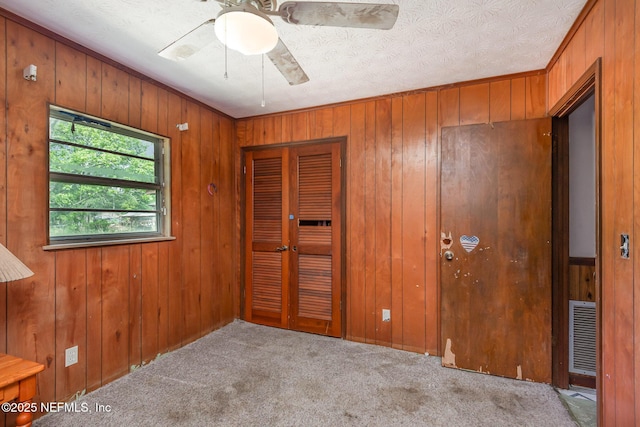 interior space with ceiling fan, carpet floors, wood walls, visible vents, and a closet