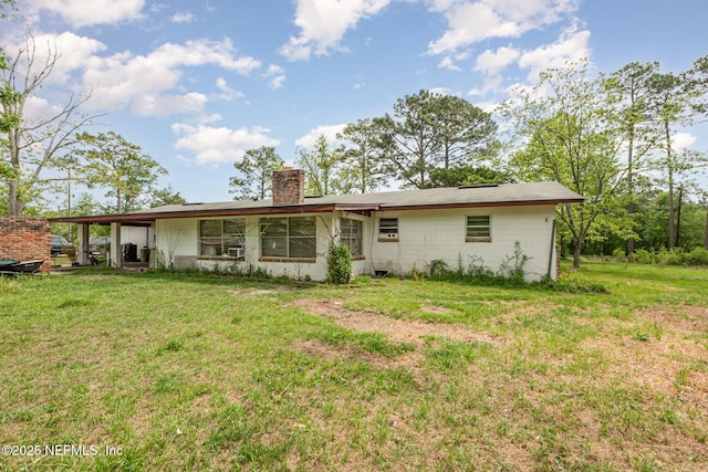 back of house with a yard, a chimney, and concrete block siding