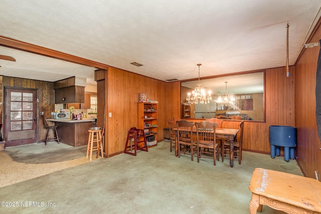 dining area with a notable chandelier, wood walls, baseboards, and visible vents