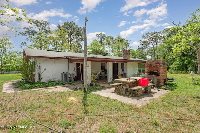 back of property featuring a patio, a lawn, a chimney, and an outdoor brick fireplace
