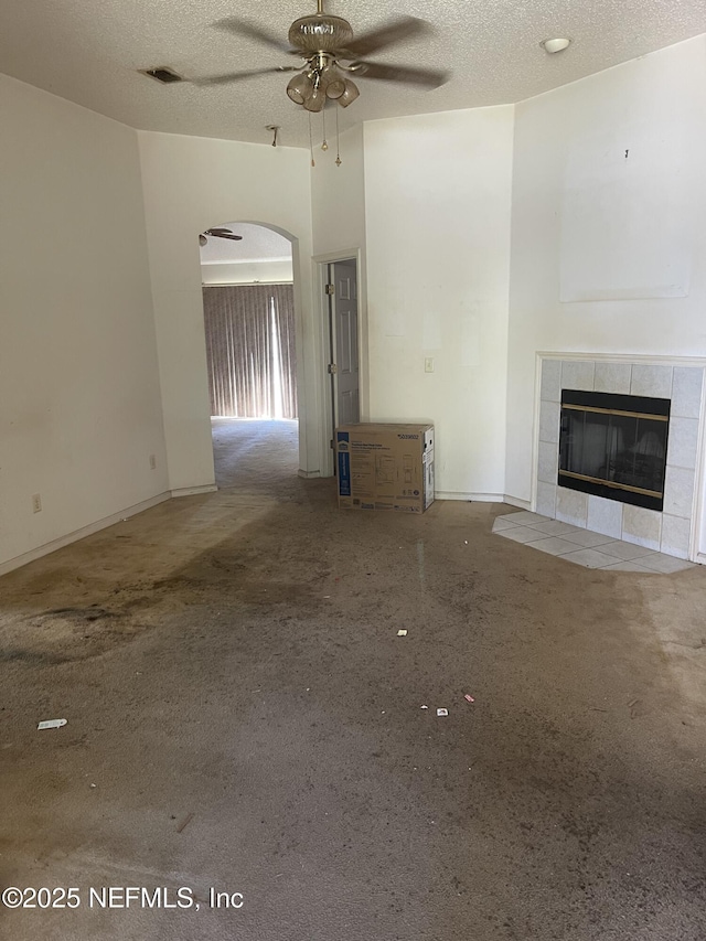 2990 Brittany Bluff Dr, Orange Park, FL 32073 - unfurnished living room with ceiling fan, a textured ceiling, a tiled fireplace, arched walkways, and carpet floors