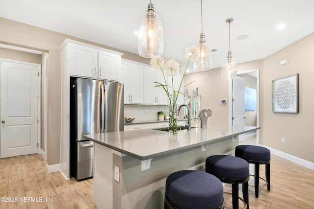 kitchen with freestanding refrigerator, a breakfast bar, baseboards, a center island with sink, and a sink