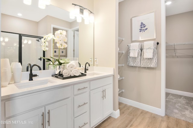 bathroom featuring a sink, a walk in closet, a shower stall, and wood finished floors