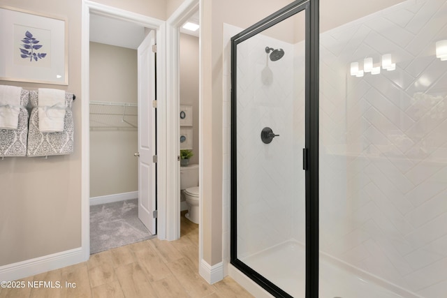 full bath featuring toilet, baseboards, wood finished floors, a spacious closet, and a stall shower
