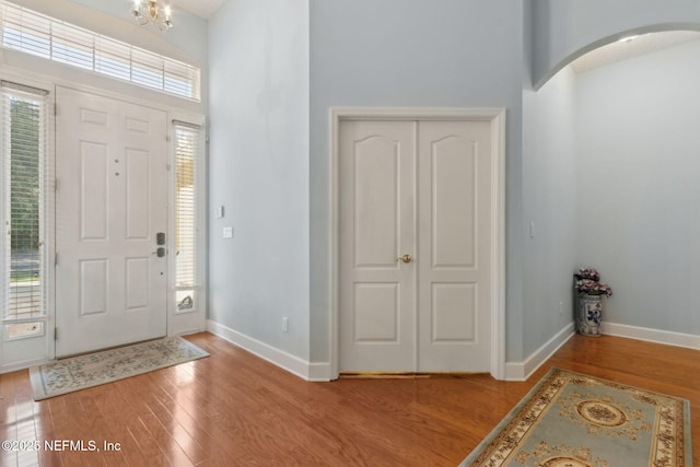 foyer entrance with light wood-style floors, arched walkways, baseboards, and a high ceiling