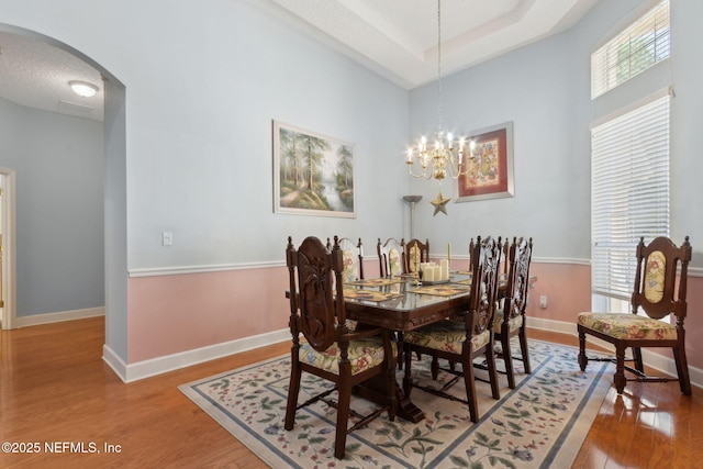 dining space featuring arched walkways, wood finished floors, baseboards, a raised ceiling, and a notable chandelier
