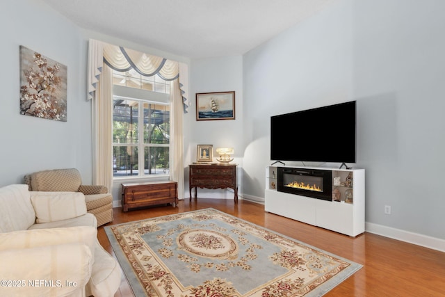 living area with baseboards, a glass covered fireplace, and wood finished floors