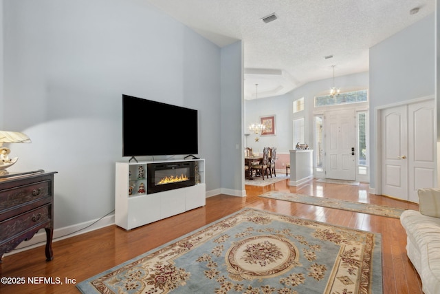 entryway featuring a textured ceiling, visible vents, wood finished floors, a chandelier, and a glass covered fireplace
