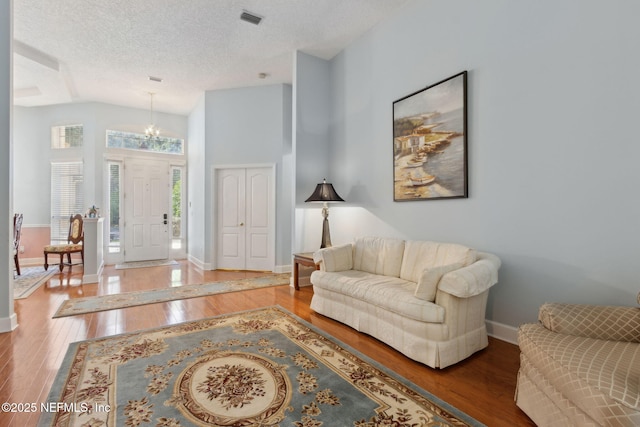 living area featuring a textured ceiling, baseboards, wood finished floors, lofted ceiling, and visible vents