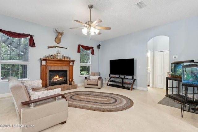 living room with a ceiling fan, visible vents, arched walkways, a brick fireplace, and carpet floors