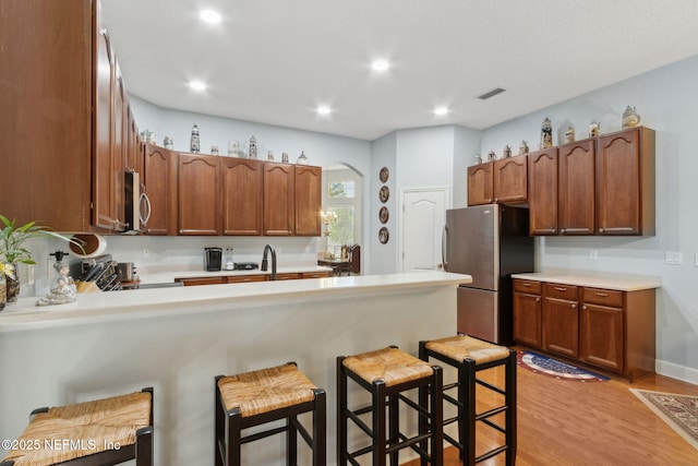 kitchen with visible vents, arched walkways, light wood finished floors, a peninsula, and stainless steel appliances