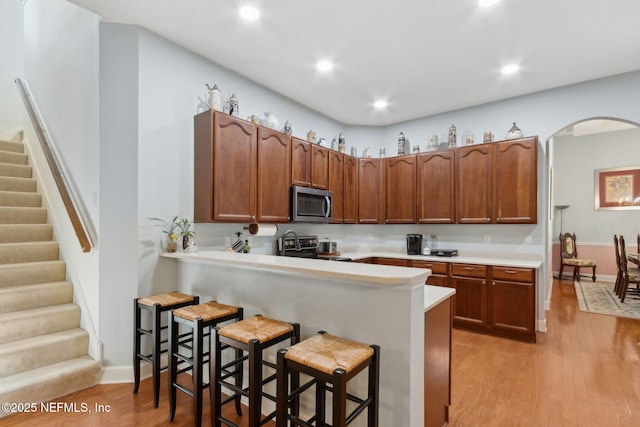 kitchen featuring a kitchen bar, light countertops, arched walkways, light wood finished floors, and stainless steel appliances