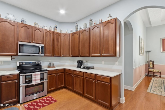 kitchen with light wood-style floors, arched walkways, light countertops, and stainless steel appliances