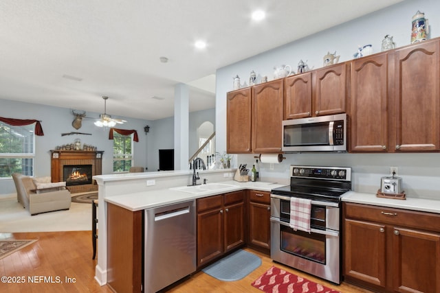 kitchen with a glass covered fireplace, ceiling fan, a sink, light wood-style flooring, and appliances with stainless steel finishes