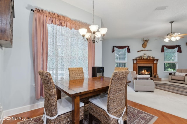 dining area with visible vents, a fireplace, wood finished floors, baseboards, and ceiling fan with notable chandelier