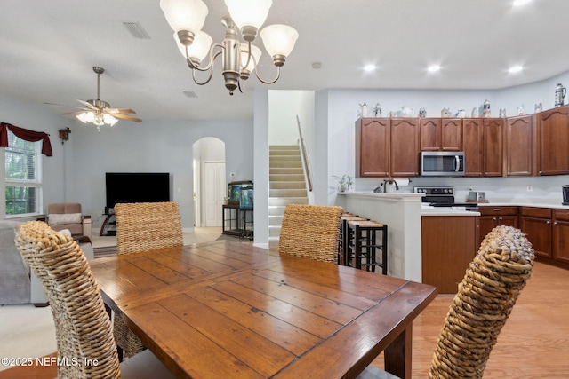 dining space featuring light wood finished floors, arched walkways, ceiling fan with notable chandelier, stairs, and recessed lighting
