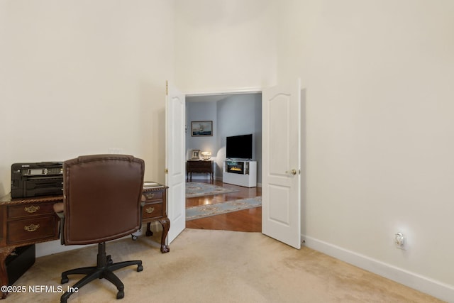carpeted office space featuring baseboards and a towering ceiling