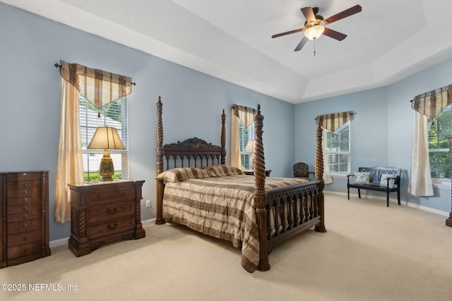 carpeted bedroom with baseboards, a ceiling fan, a raised ceiling, and multiple windows