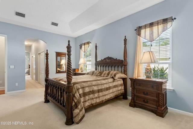 bedroom featuring arched walkways, multiple windows, visible vents, and light colored carpet