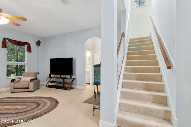 interior space featuring arched walkways, carpet, a ceiling fan, and a textured ceiling