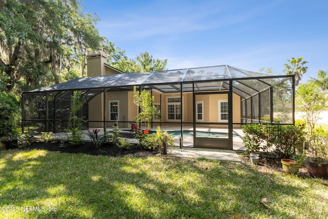 back of property with glass enclosure, stucco siding, a yard, and a chimney