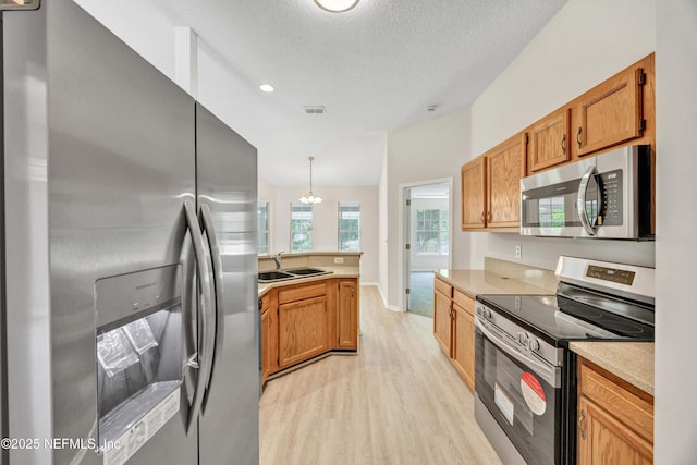 kitchen with appliances with stainless steel finishes, a sink, light countertops, a peninsula, and light wood-style floors
