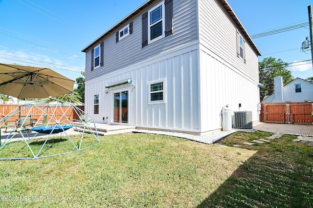 back of property with central air condition unit, a fenced backyard, a yard, and board and batten siding