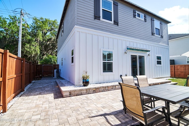 rear view of house with board and batten siding, a patio, a fenced backyard, and outdoor dining space