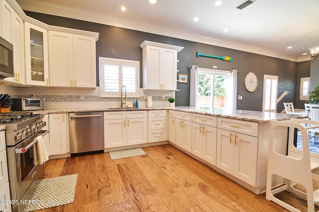 kitchen featuring a sink, a peninsula, stainless steel appliances, visible vents, and crown molding