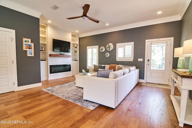 living room featuring ornamental molding, light wood-type flooring, visible vents, a fireplace, and a ceiling fan