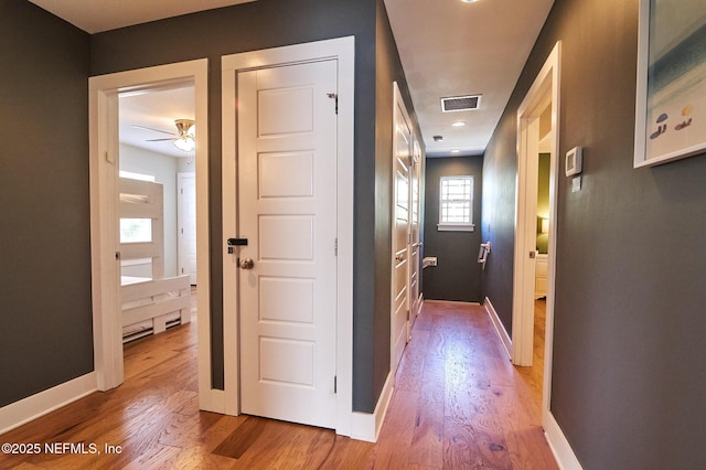 hallway featuring visible vents, wood finished floors, and baseboards