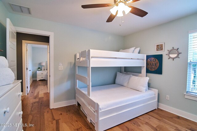 bedroom featuring baseboards, ceiling fan, visible vents, and wood finished floors