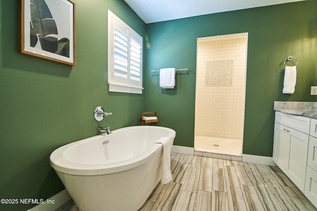 full bathroom featuring a freestanding bath, vanity, baseboards, and tiled shower