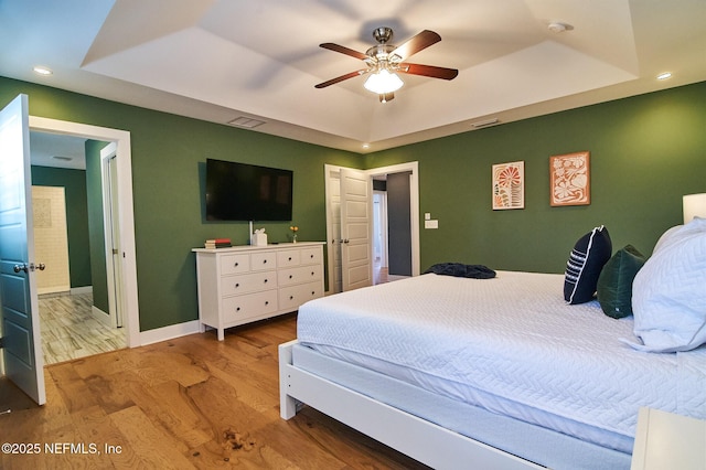 bedroom with wood finished floors, a tray ceiling, visible vents, baseboards, and recessed lighting