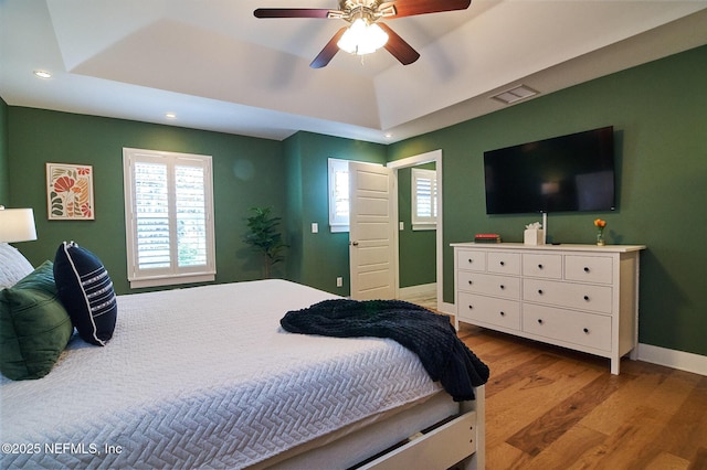 bedroom featuring a tray ceiling, recessed lighting, baseboards, and wood finished floors