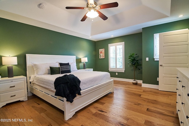 bedroom featuring a tray ceiling, baseboards, light wood-style flooring, and recessed lighting