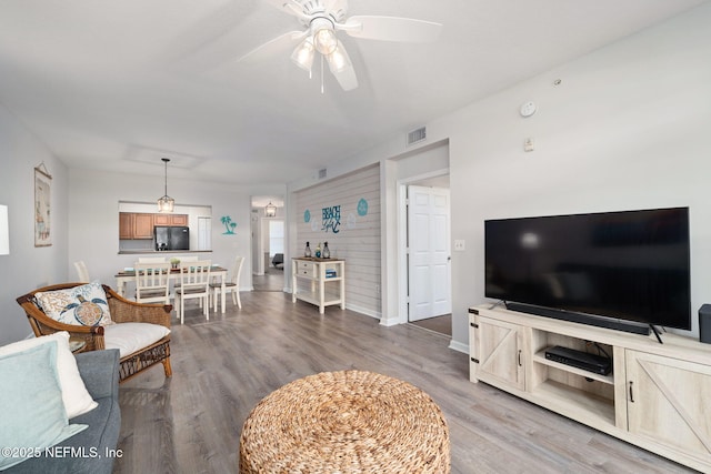 living area with baseboards, ceiling fan, wood finished floors, and visible vents