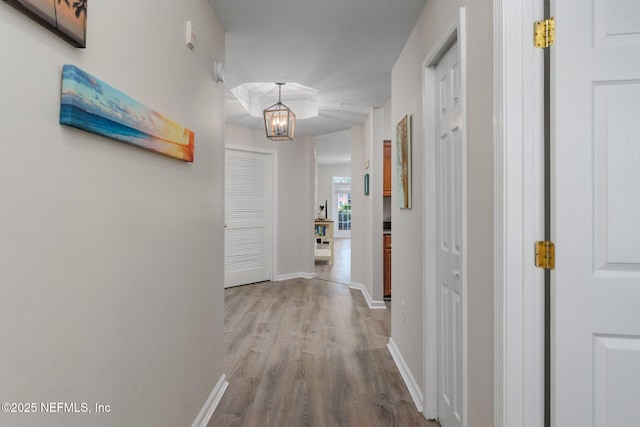 hall with baseboards, wood finished floors, and a notable chandelier